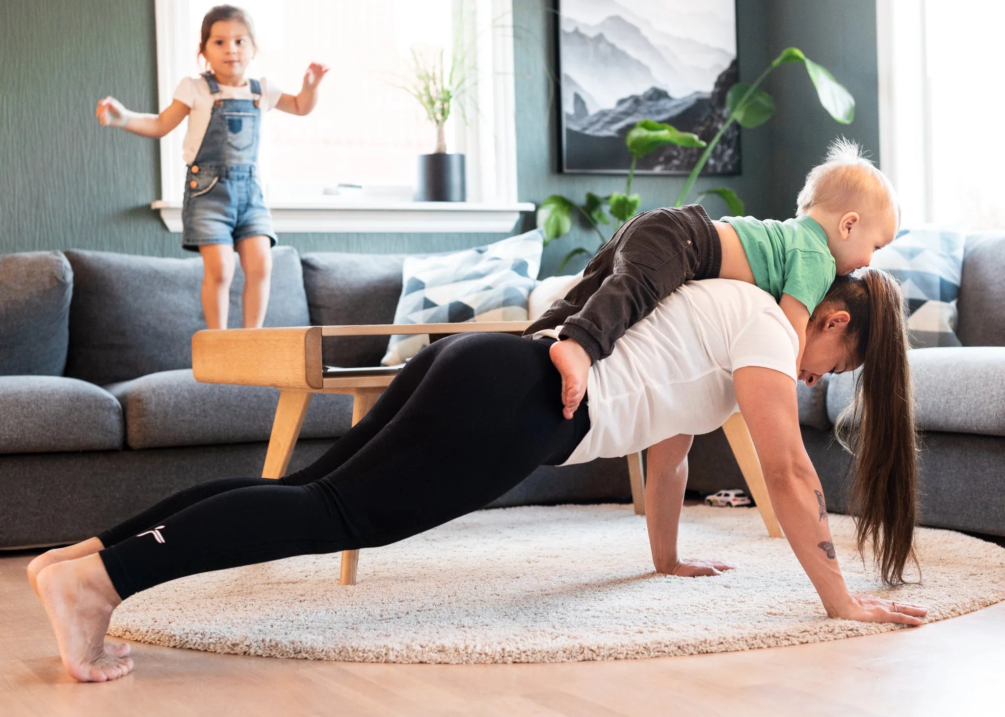 Woman doing a plank with a child on her back in a living room.